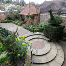 View down into the Godalming Museum's Getrude Jekyll-inspired garden showing brick paving. circular steps, gazebo and topiary.