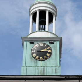 The Cupola of The Pepperpot showing the face of the clock surrounded by verdigris and the bell tower above with a background of blue sky and wispy white clouds