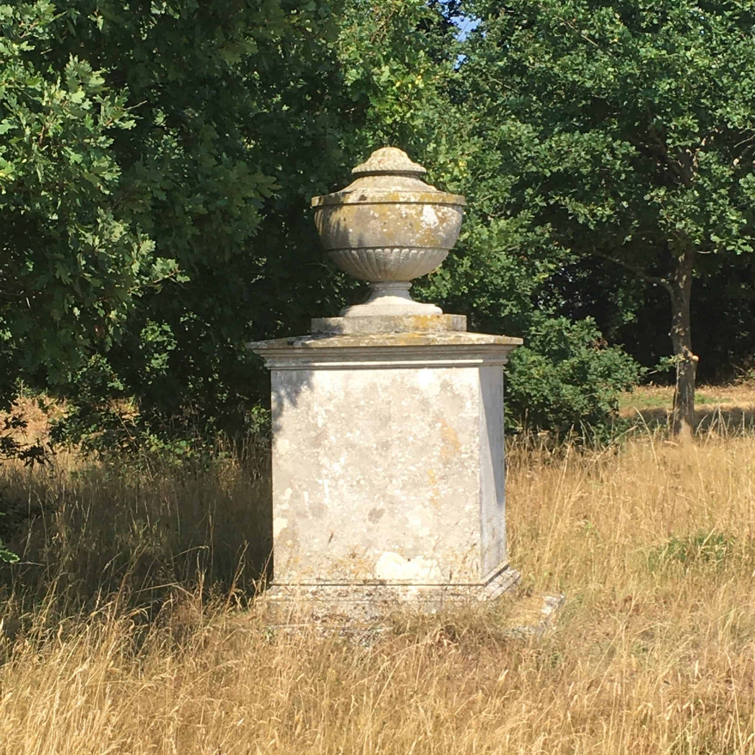 Large stone plinth with stone urn atop set amongst the trees bordering the natural burial area